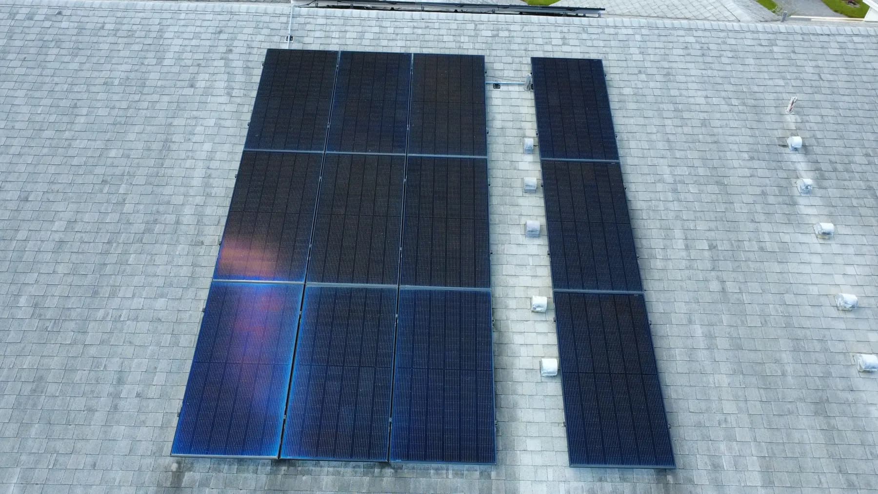 Drone view looking straight down on a twelve-panel rooftop solar array on a gray shingle roof.